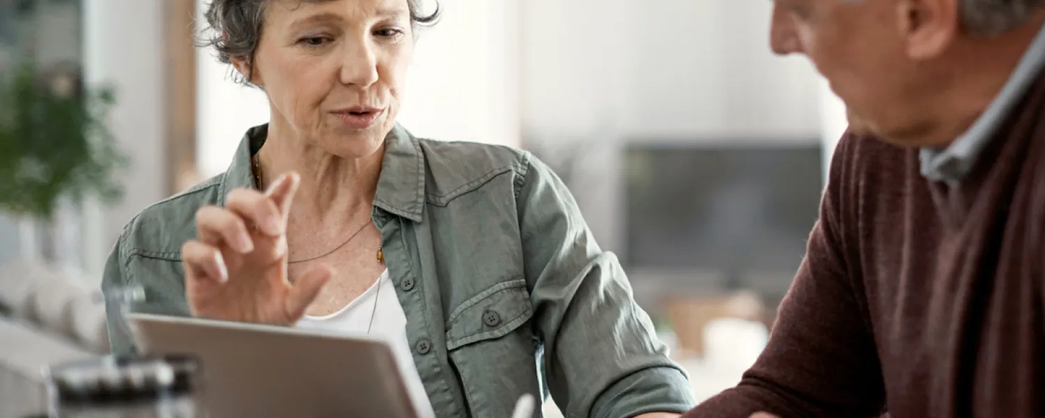 This image captures an older couple engaging in a conversation, sharing and discussing information they've found online with each other.