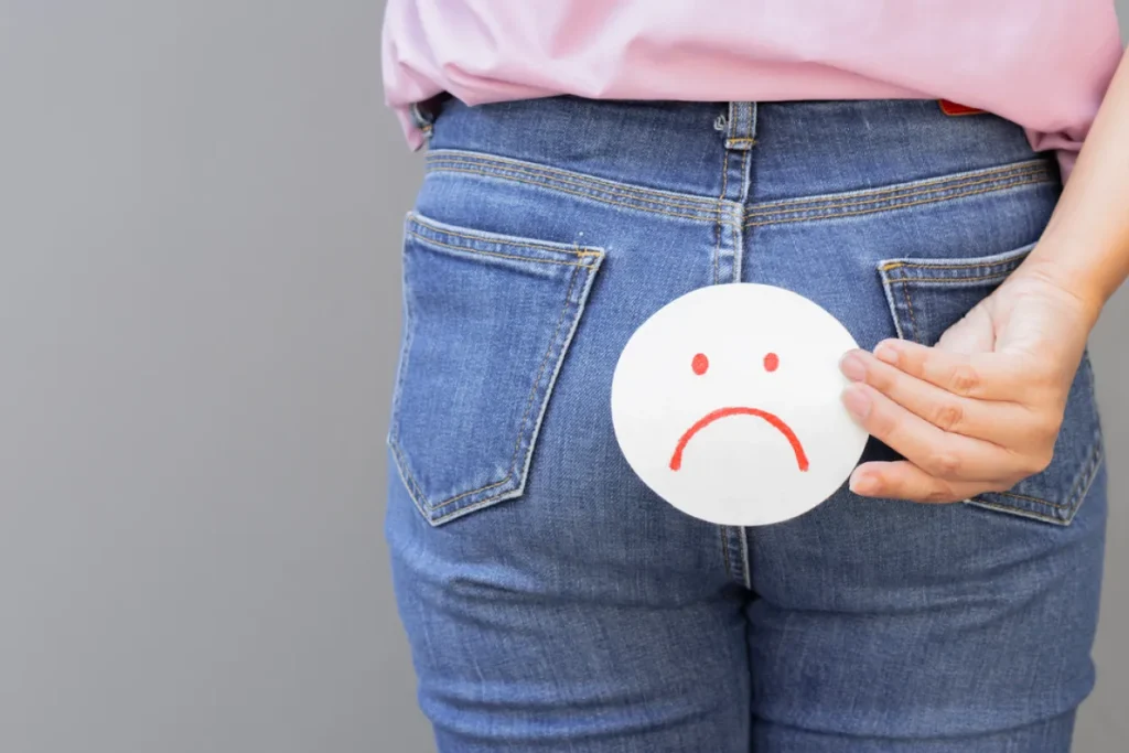 Image of a person holding a sad face icon over their butt, illustrating symptoms like bloody diarrhea, bloody stool, severe diarrhea with blood, causes and diagnosing bloody diarrhea.