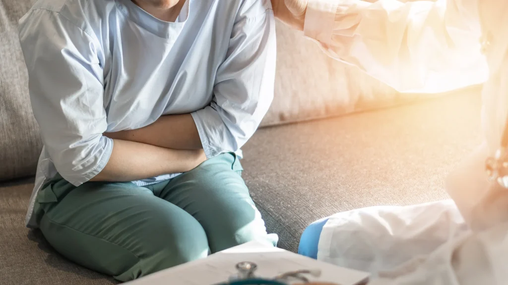 A person sitting on a couch, clutching their stomach in discomfort, caused by diarrhea and inflammation