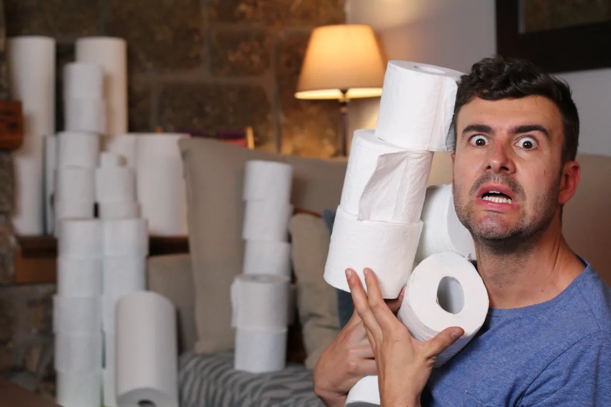 Image of a concerned, panicked-looking man holding piles of toilet paper, illustrating symptoms like explosive diarrhea, severe diarrhea symptoms, causes of sudden diarrhea, acute diarrhea treatment, intestinal infection signs, and chronic diarrhea remedies.