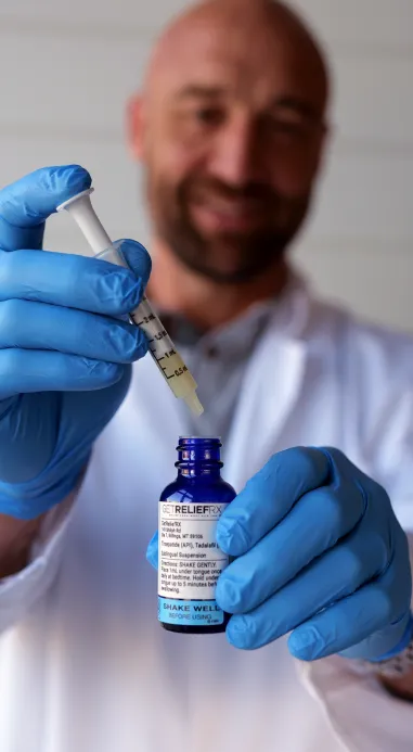 A man wearing a smock and gloves holding a prescription medication and a syringe.