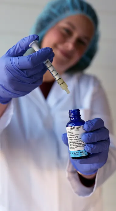 A female pharmacy technician demonstrates holding a bottle of Semaglutide while also holding an oral syringe.