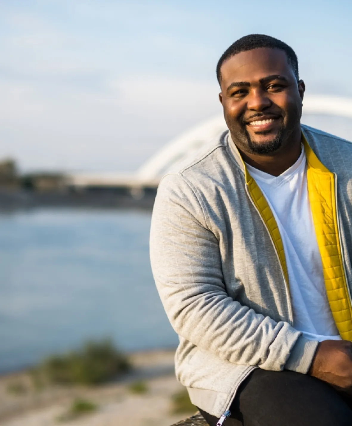 A man sits in front of a river and smiles at the camera.