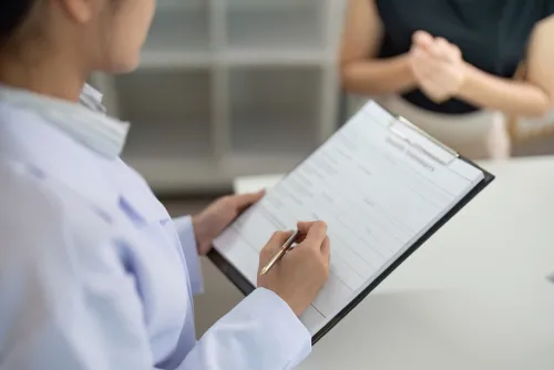 A medical provider takes notes on a chart while giving a consultation to a patient.